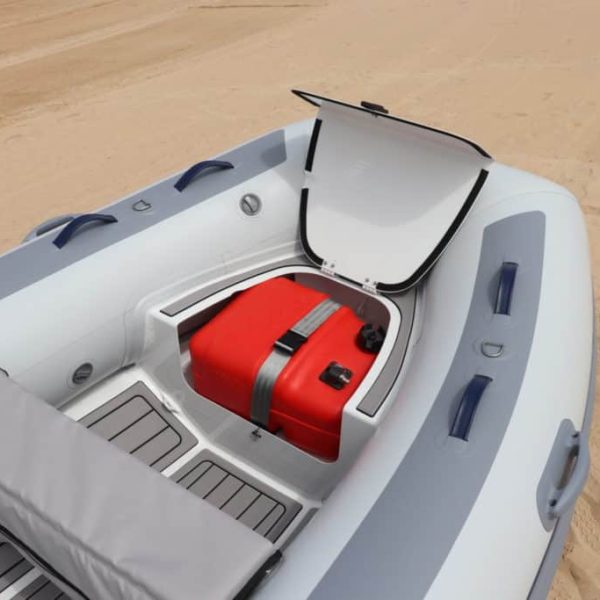Interior de un bote inflable con un compartimento que contiene un tanque de combustible rojo, sobre una superficie de arena.