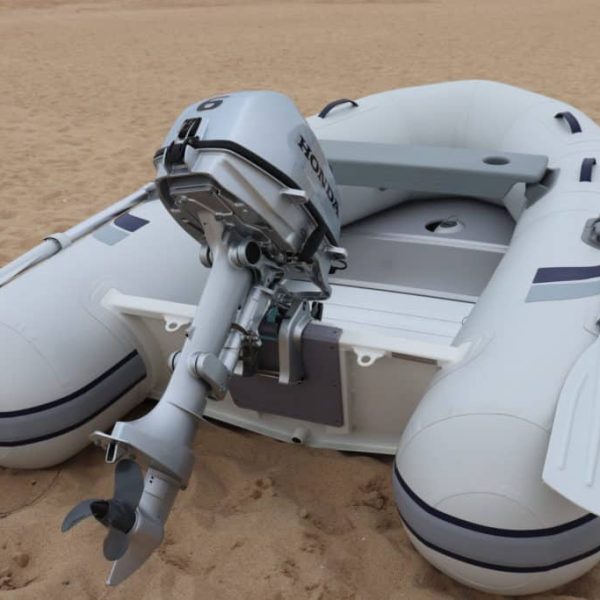 Bote inflable de color blanco con motor Honda en la playa, mostrando remos y detalles de diseño. Ideal para actividades acuáticas y navegación.