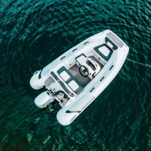 Bote inflable blanco sobre aguas cristalinas, con asientos cómodos y timón, ideal para actividades náuticas y paseos en el mar.