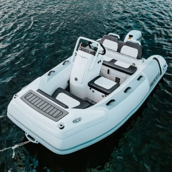 Bote inflable Highfield blanco sobre aguas tranquilas, con asientos en la parte interior y motor Honda en la parte trasera. Ideal para actividades acuáticas y excursiones.