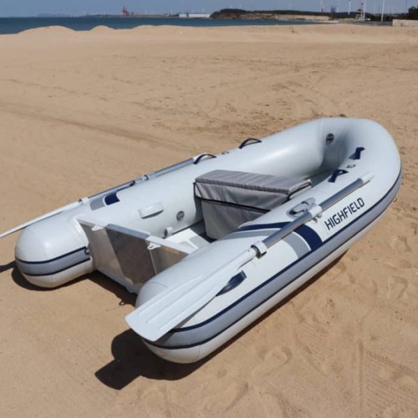 Bote inflable Highfield en una playa de arena, listo para la navegación, con el mar y un paisaje costero de fondo.