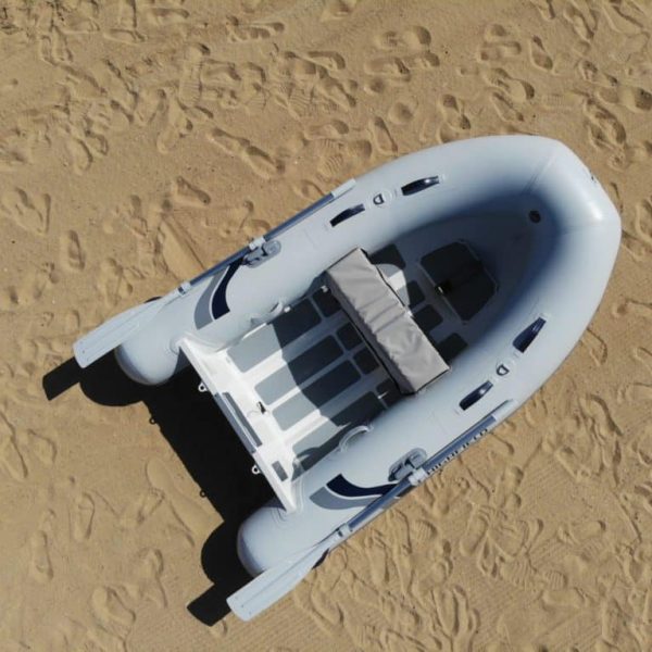 Bote inflable gris sobre arena, visto desde arriba, con un asiento central y espacio para varios ocupantes, ideal para actividades acuáticas y exploración.
