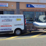 Furgoneta de Honda Marine estacionada frente a una tienda de náutica en Las Palmas, con un bote inflable de la marca Highfield enganchado. Se observan detalles de la tienda y el logotipo de Beta Marine.