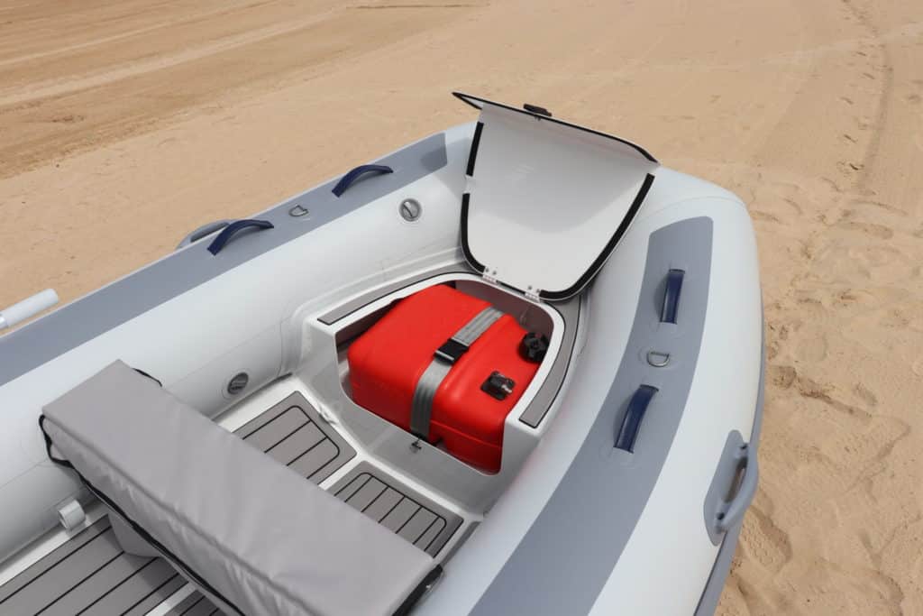 Interior de un bote inflable con un compartimento que contiene un tanque de combustible rojo, sobre una superficie de arena.