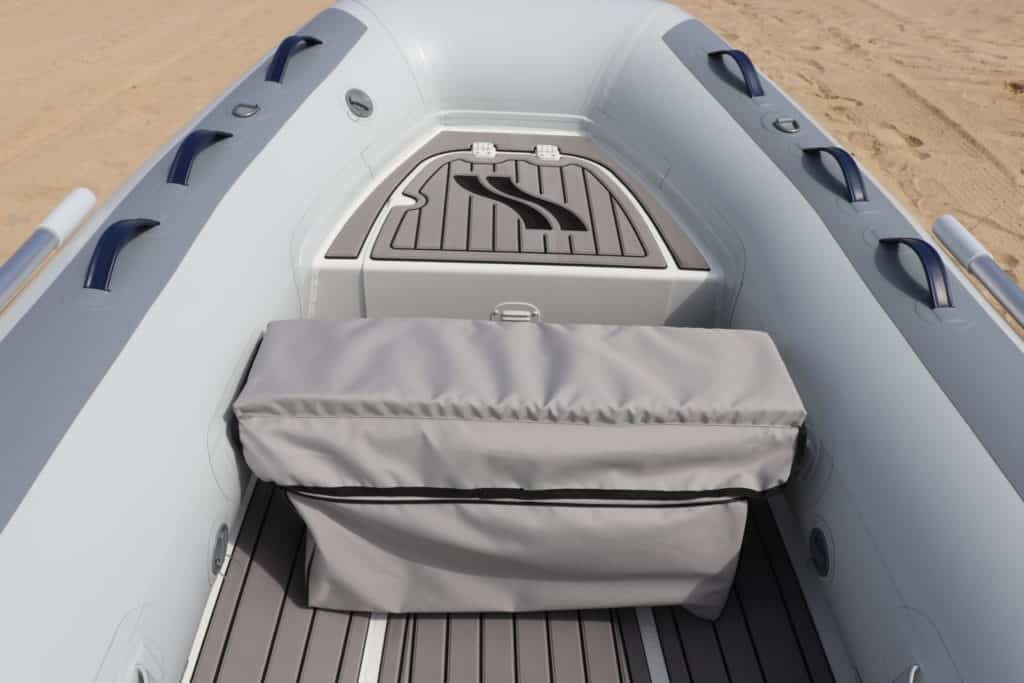 Interior de una lancha inflable con un banco de almacenamiento gris y un fondo de cubierta antideslizante. Ideal para actividades acuáticas y paseos en el mar.