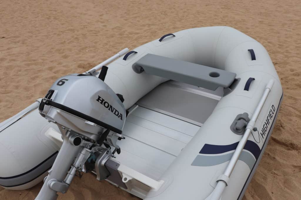 Bote inflable Highfield con motor Honda en una playa de arena. El bote presenta un diseño cómodo y funcional, ideal para actividades acuáticas y navegación.