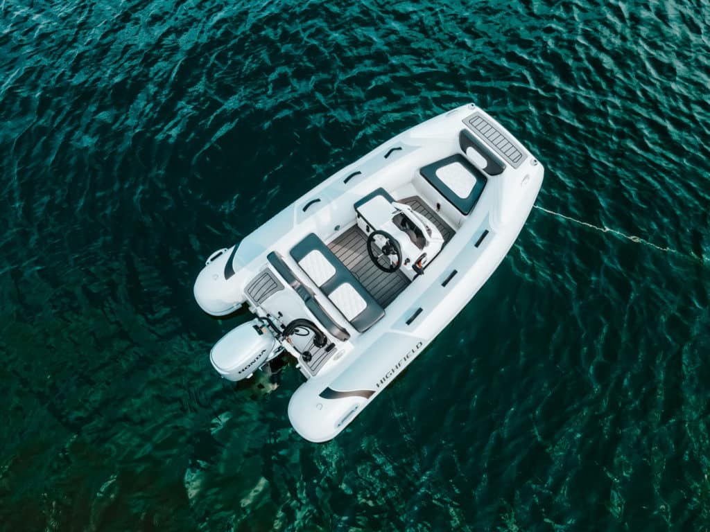 Bote inflable blanco sobre aguas cristalinas, con asientos cómodos y timón, ideal para actividades náuticas y paseos en el mar.