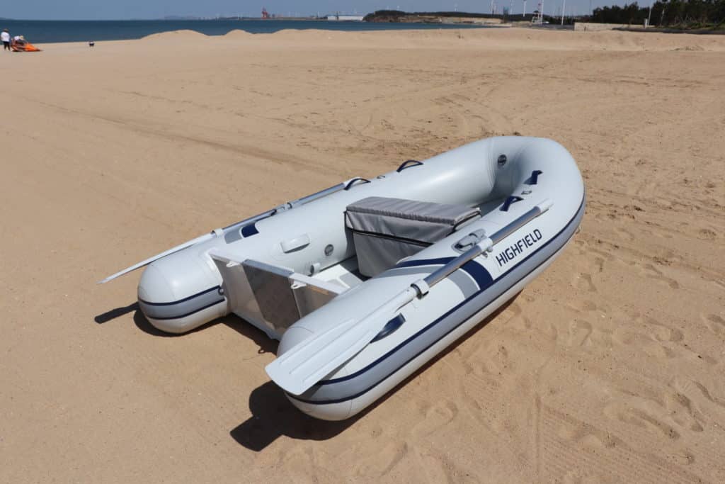 Bote inflable Highfield en una playa de arena, listo para la navegación, con el mar y un paisaje costero de fondo.