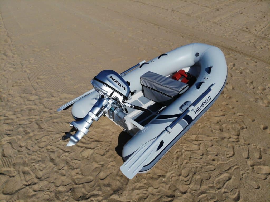 Bote inflable Highfield con motor Honda, estacionado en la arena, ideal para actividades acuáticas y exploración.
